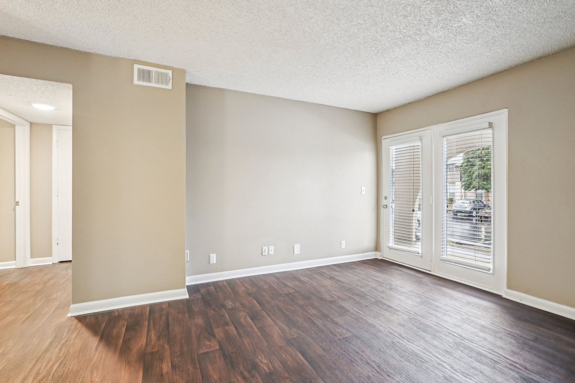 Empty room with wood-look flooring, beige walls, textured ceiling, and glass French doors leading outside.