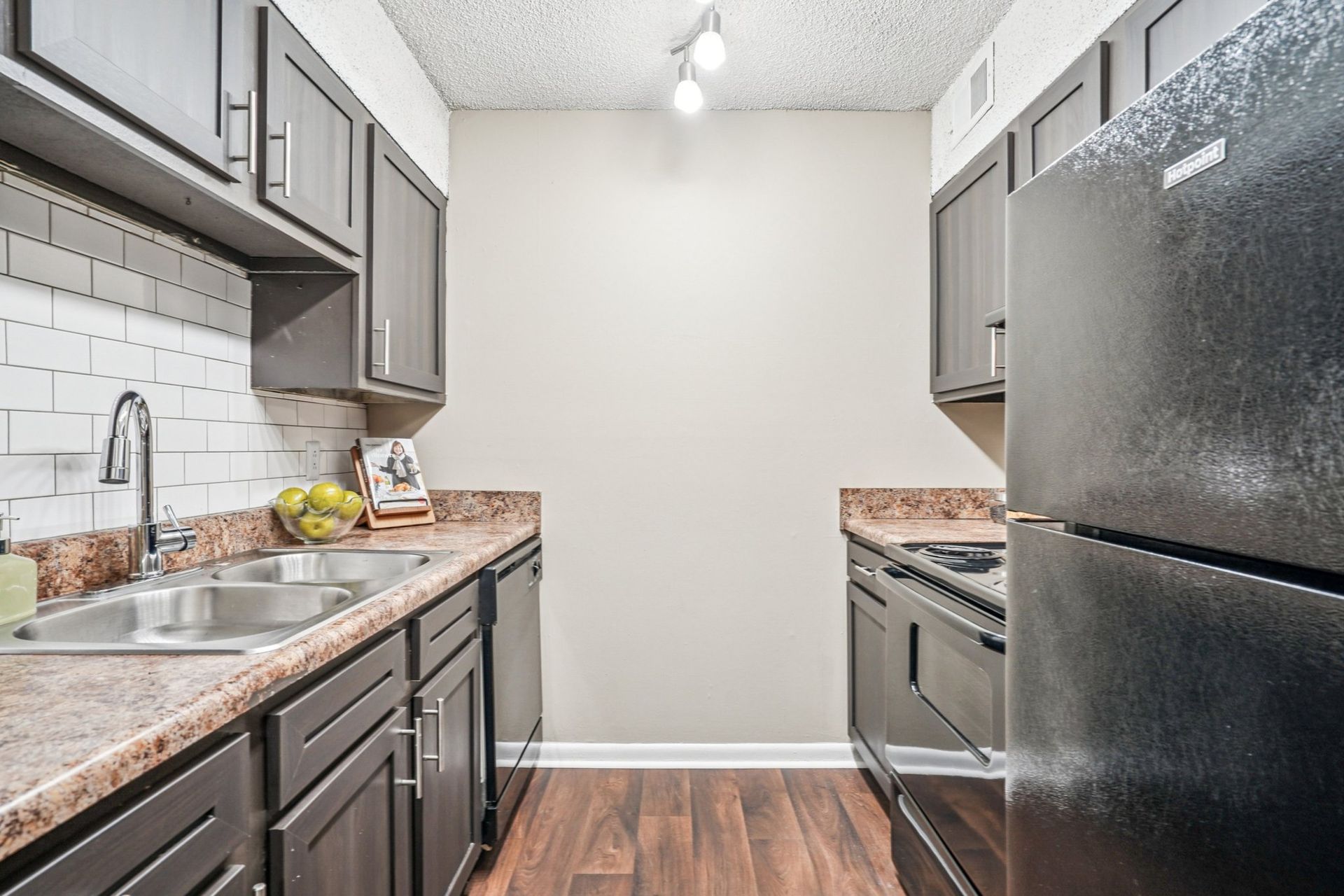 A galley-style kitchen with dark cabinetry, granite countertops, a black refrigerator, and white subway tile backsplash.