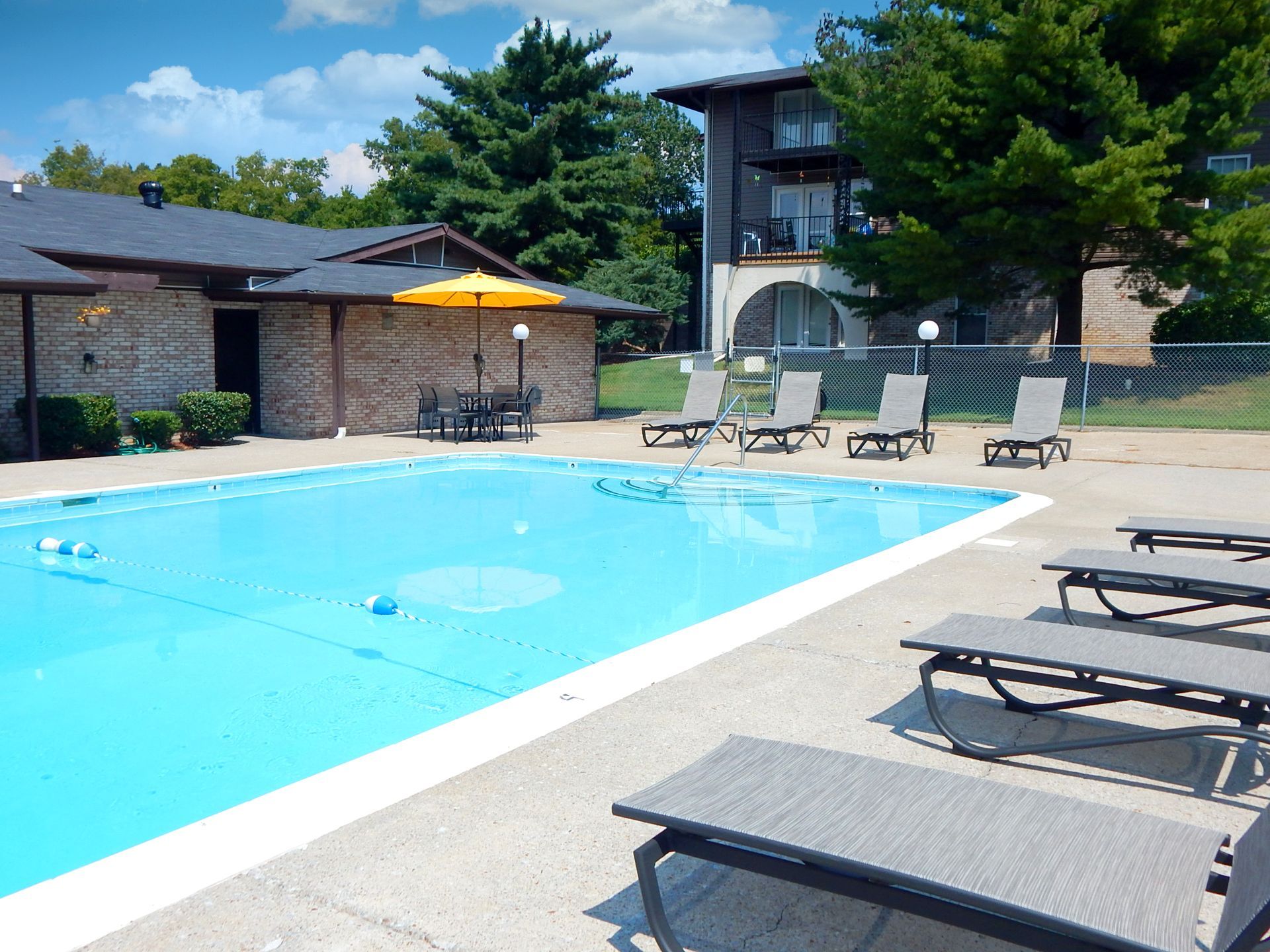 An outdoor swimming pool with lounge chairs on the patio and a nearby building with a yellow umbrella.