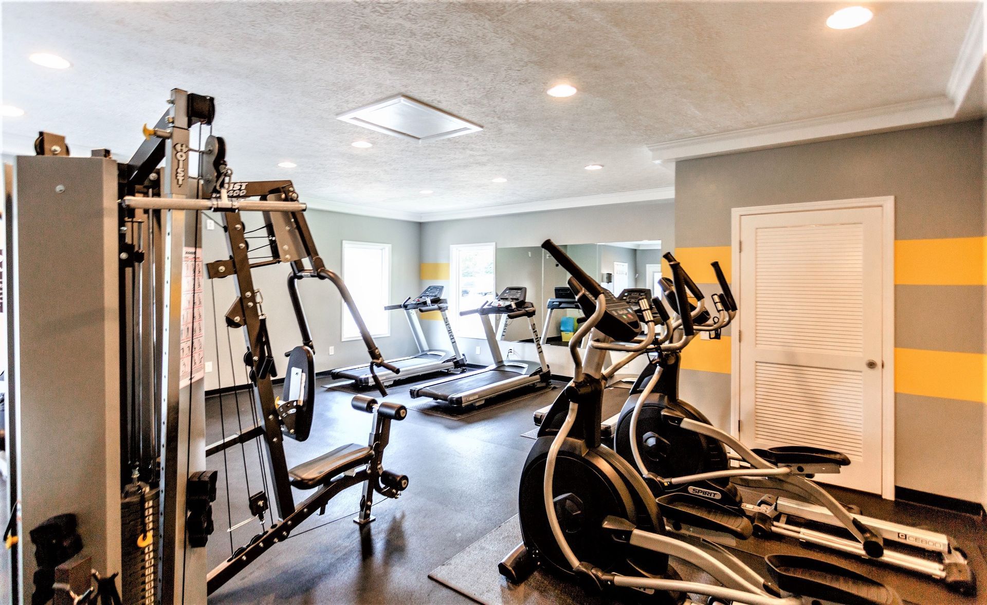 An indoor fitness center featuring a multi-station weight machine, elliptical machines, and treadmills.