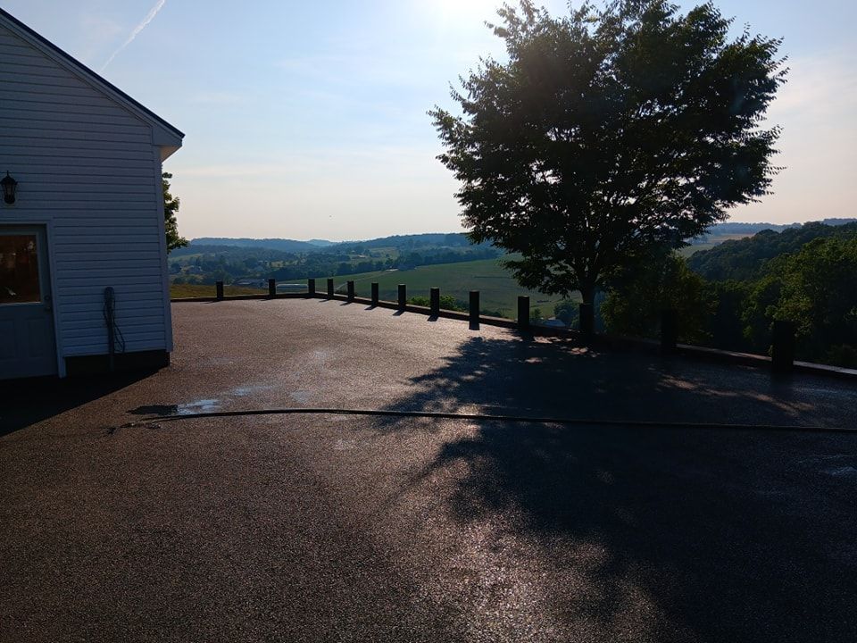 Asphalt patio with a view of a tree and rolling hills under a sunny sky.