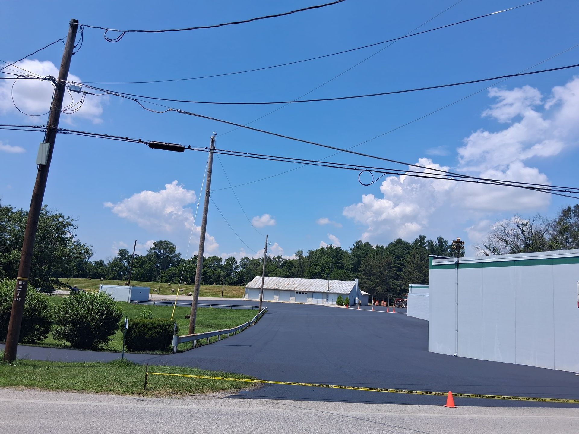 Newly paved asphalt driveway leading to white buildings under a blue sky with utility poles.