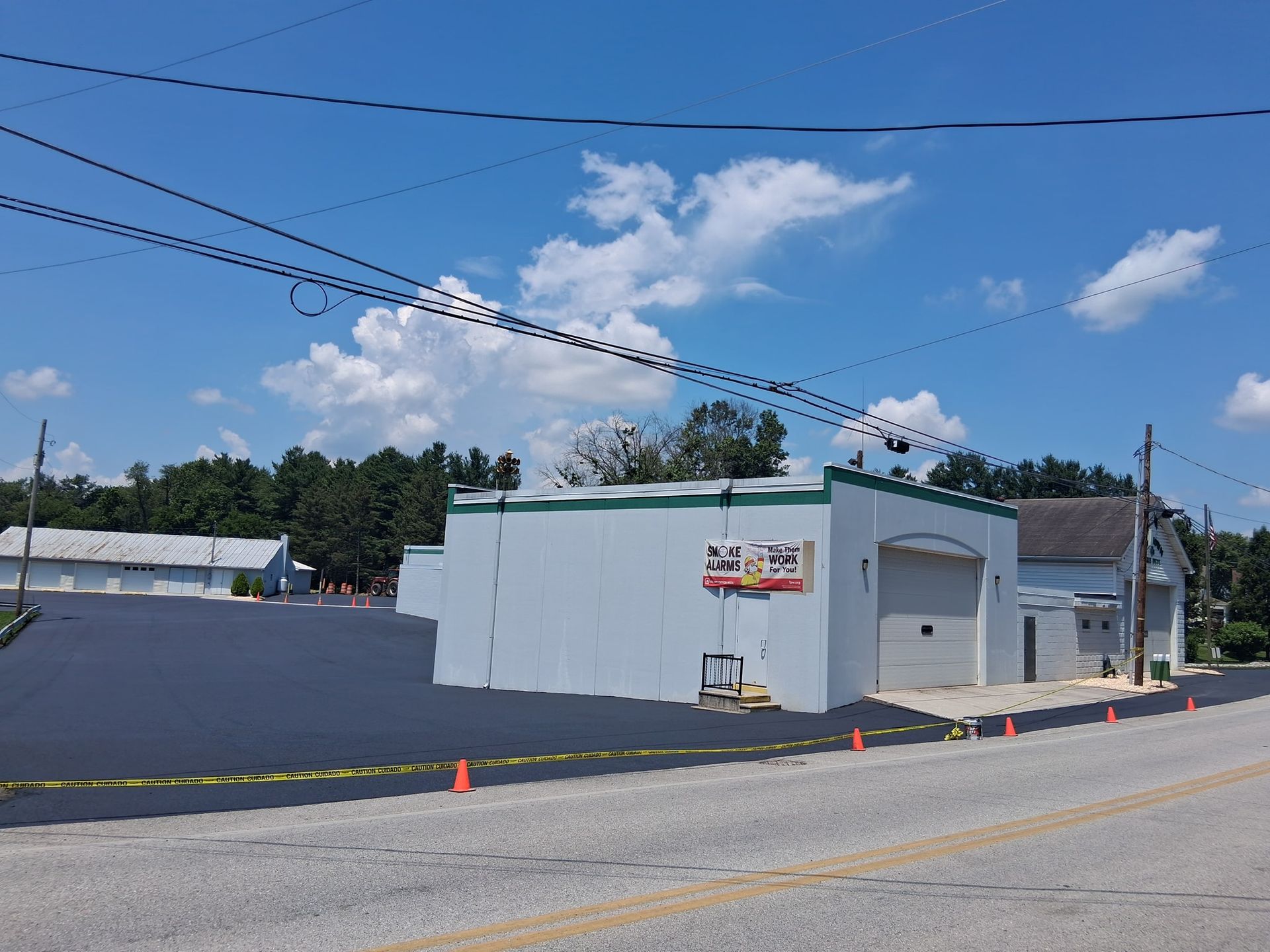 Paved road, blue sky, and a light-colored building. Power lines overhead with caution cones on the road.