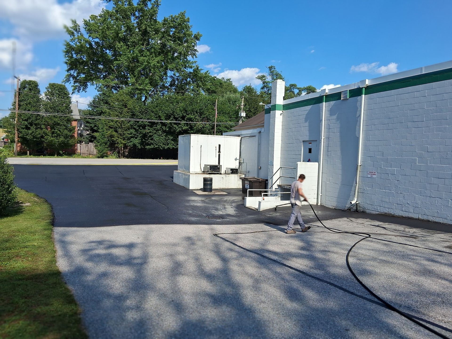 Person pressure washing a parking lot next to a white building under a blue sky.