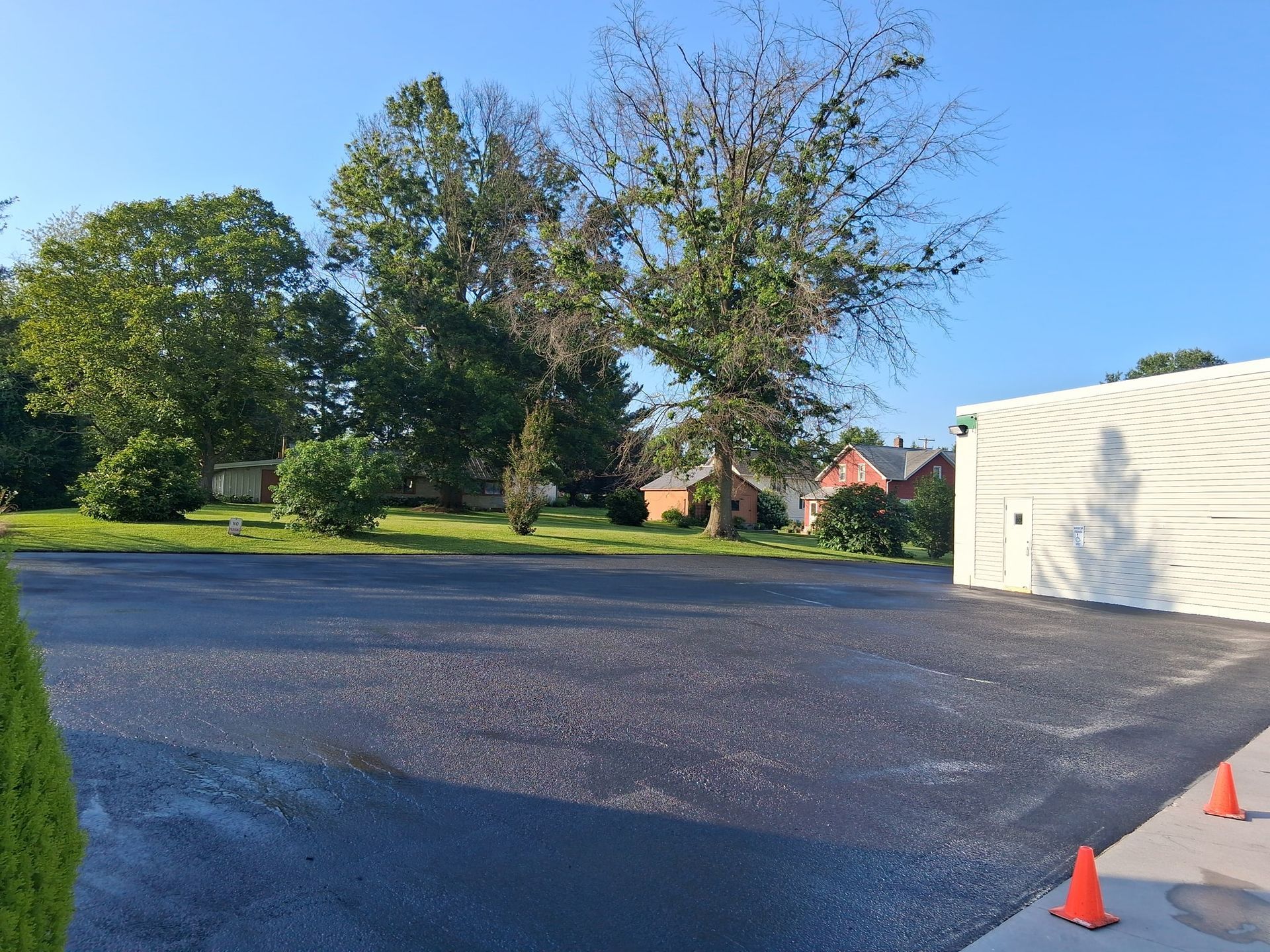 Newly paved parking lot with trees and a building on a sunny day.