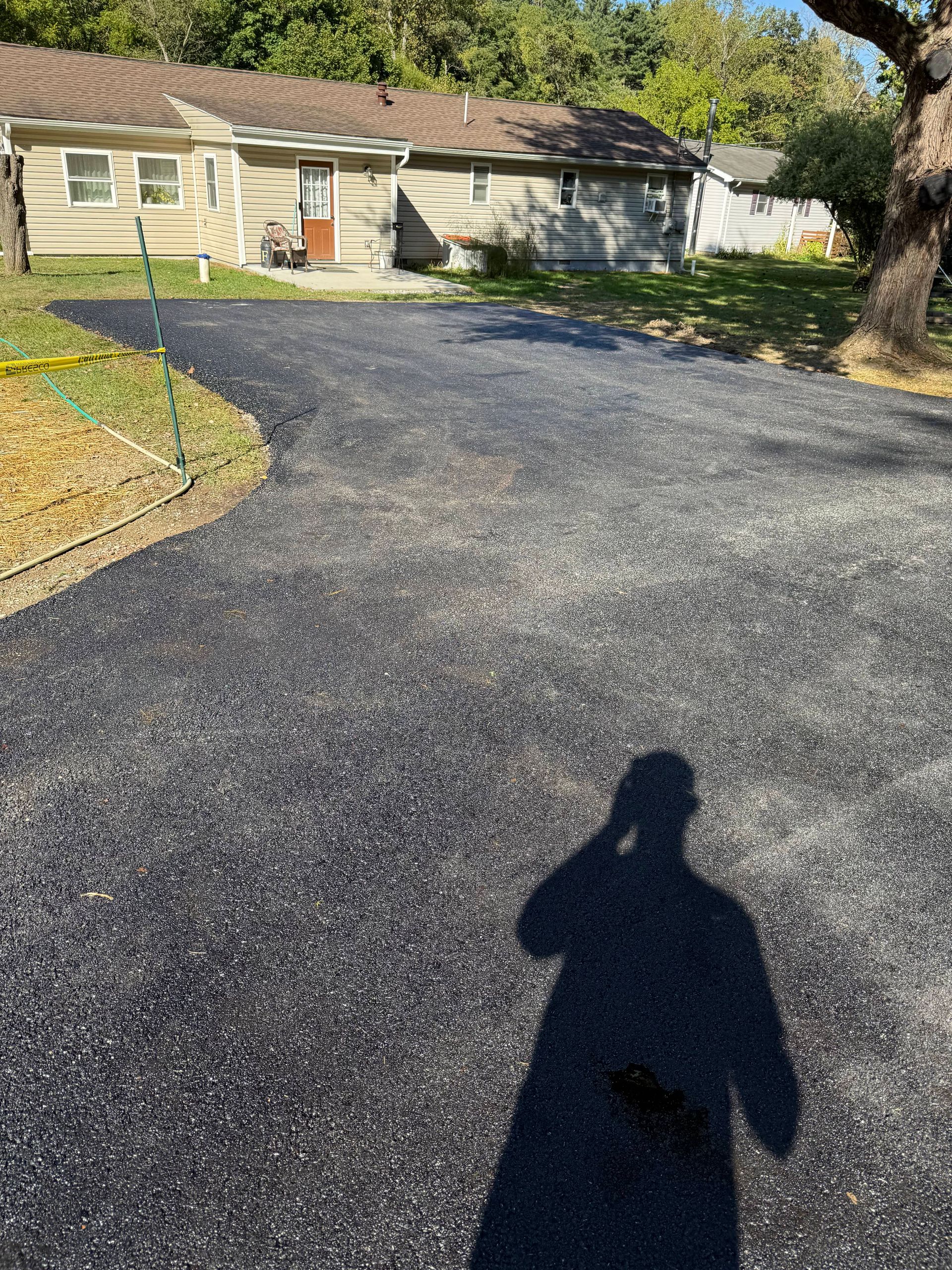 Newly paved asphalt driveway leading toward houses. Person's shadow visible on the driveway.