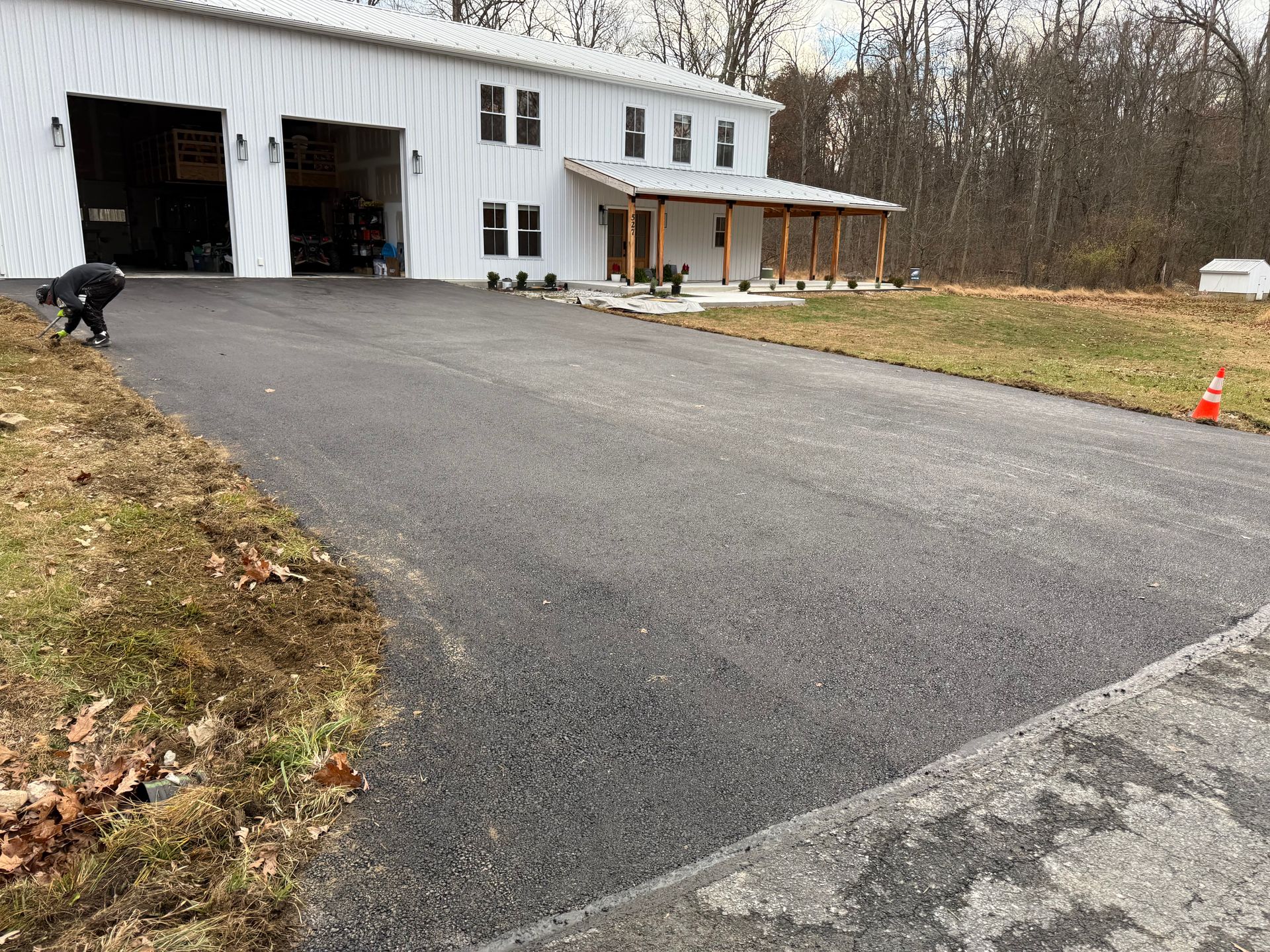 New asphalt driveway leading to a white building with a covered porch. A person is near the driveway.