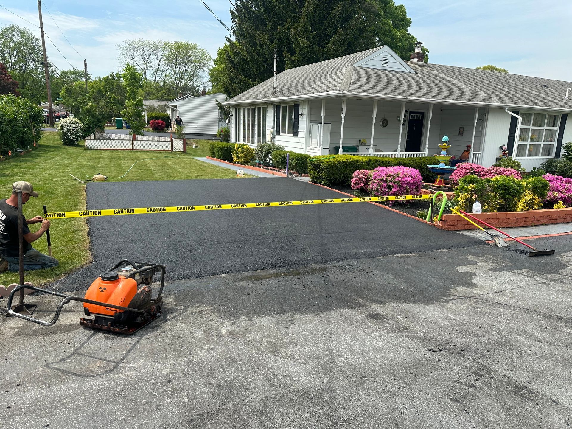 New asphalt driveway being installed in front of a white house with landscaping.