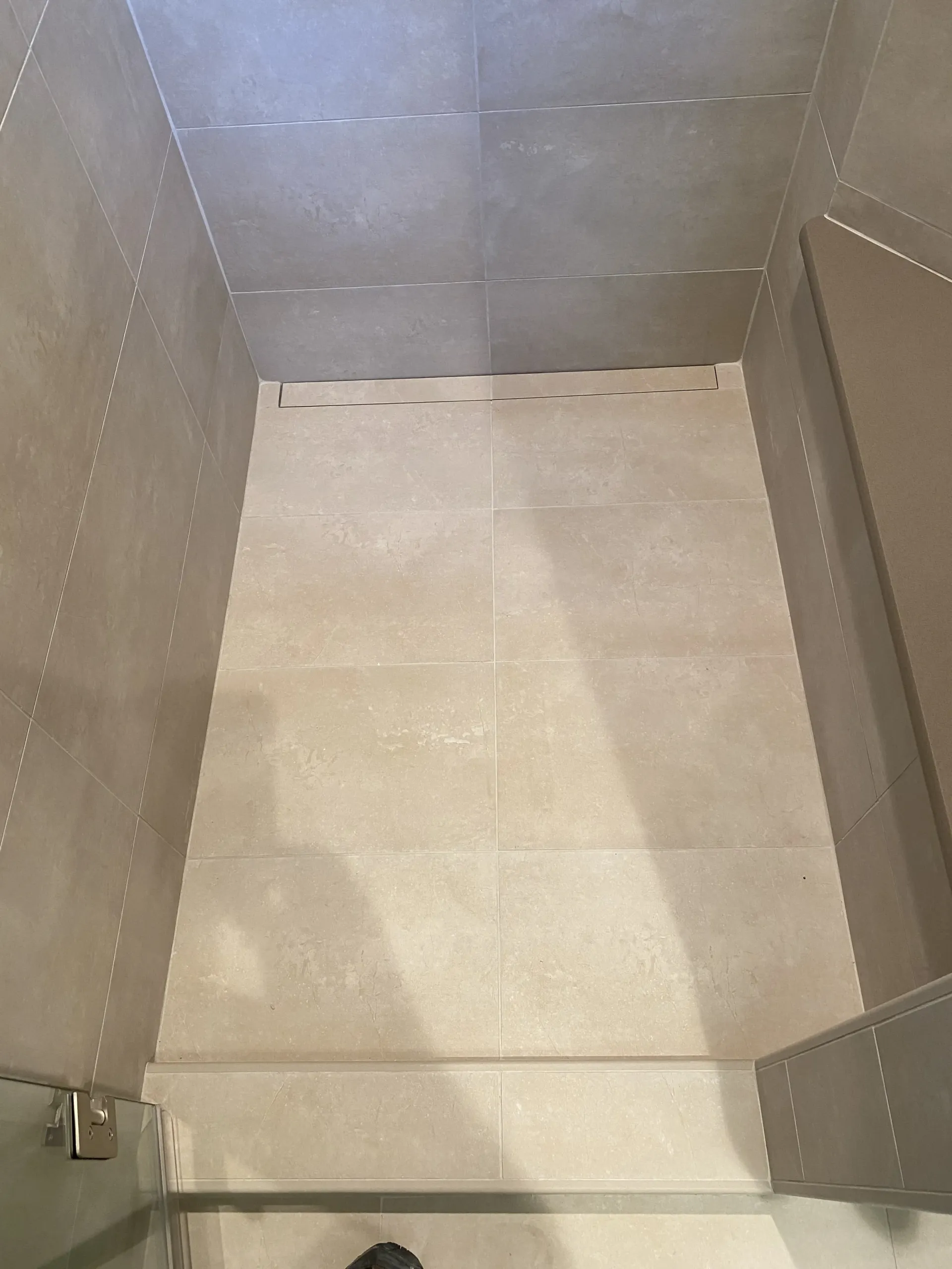 Interior view of a walk-in shower with beige floor tiles, grey wall tiles, and a built-in bench on the right side.