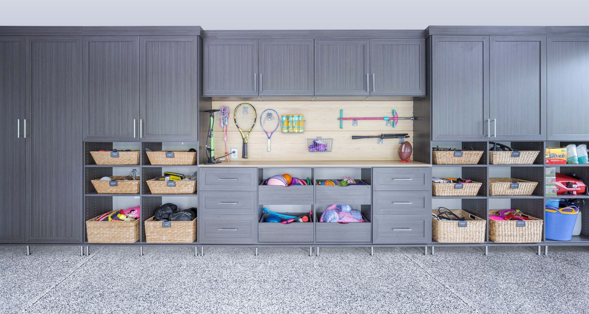Garage storage wall with gray cabinets, open bins, and children’s sports gear on shelves