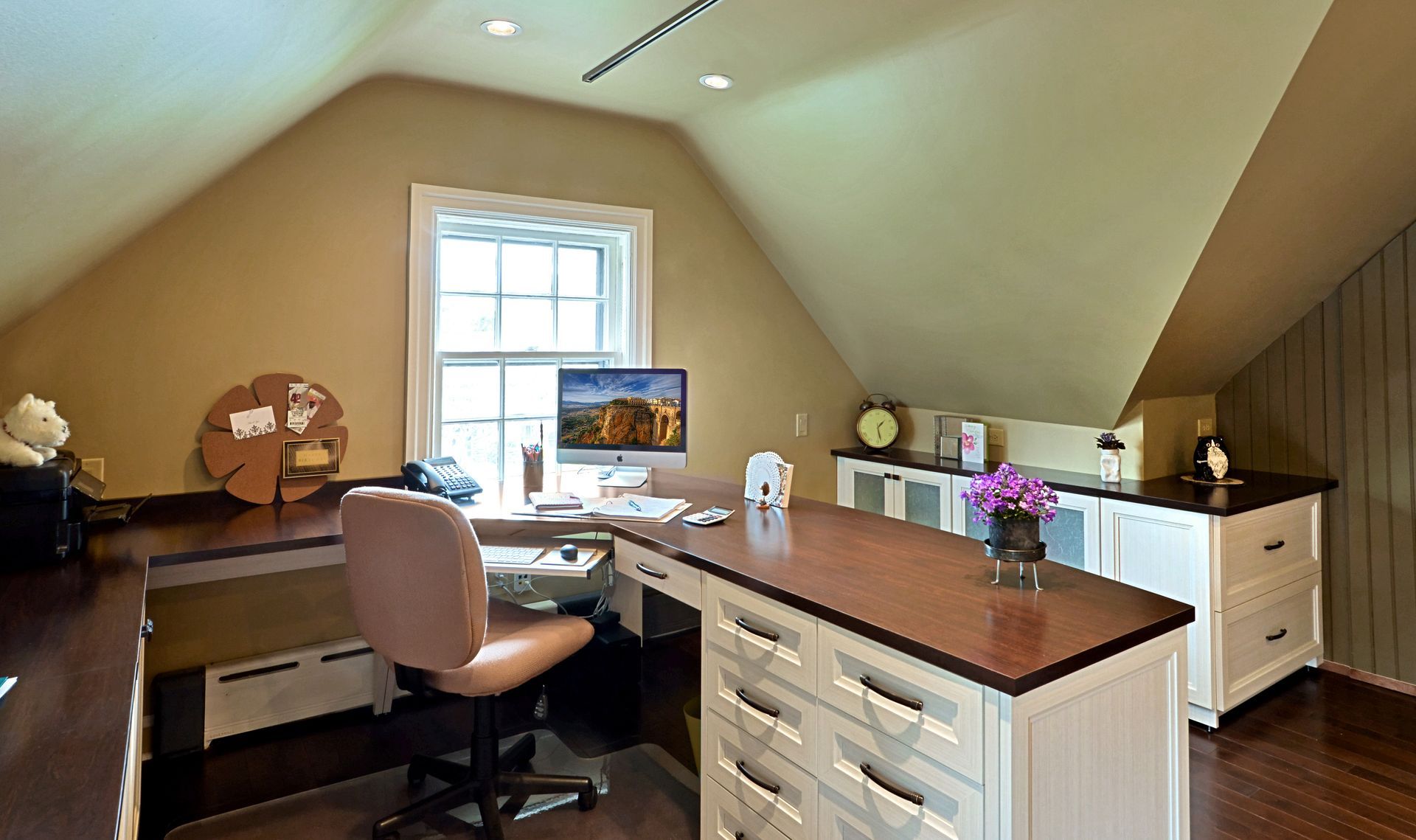 Home office with desk, computer, chair, and white storage cabinets under a sloped ceiling.