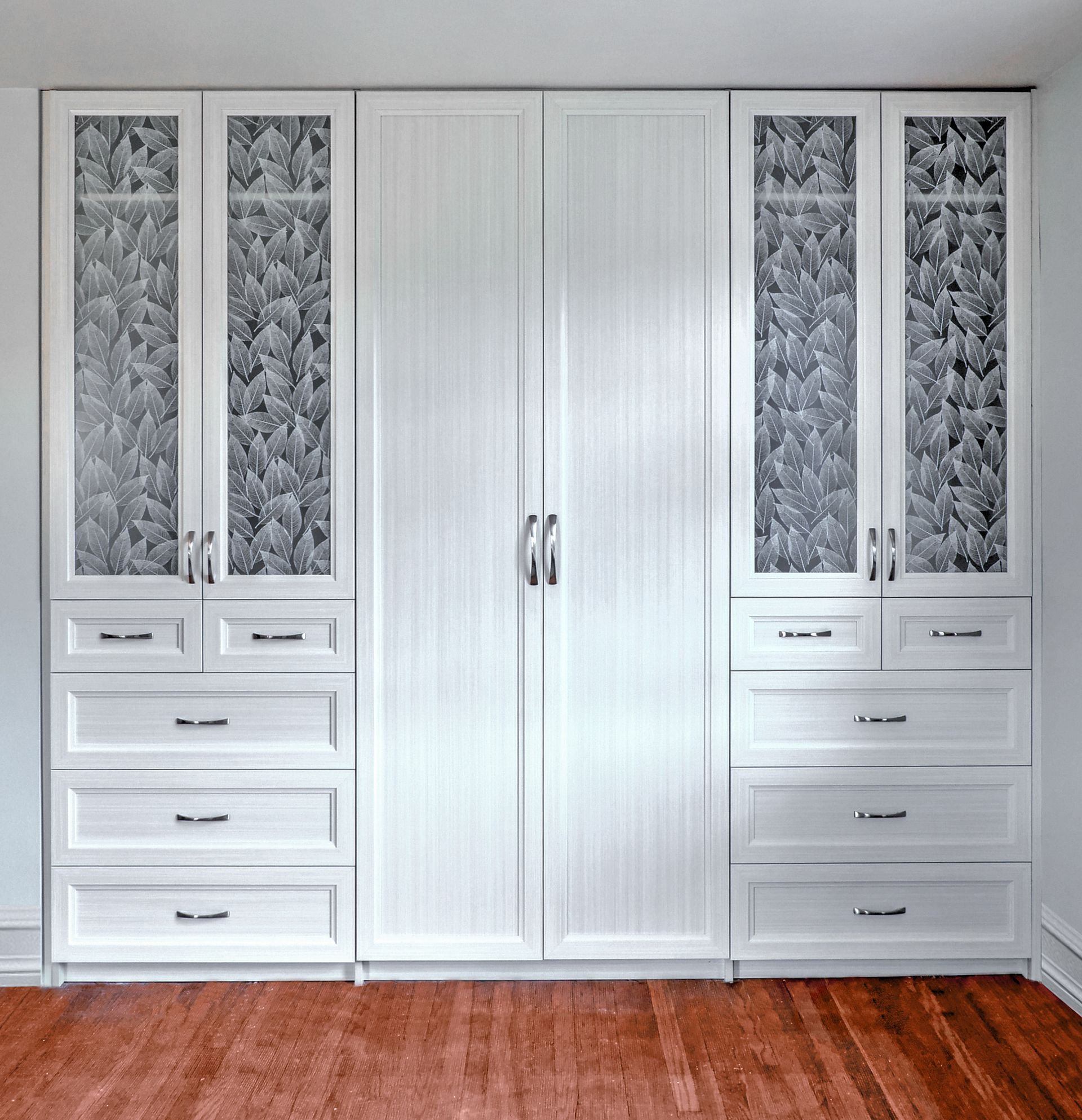 Built-in white wardrobe wall with cabinets, drawers, and frosted glass panels above a wooden floor