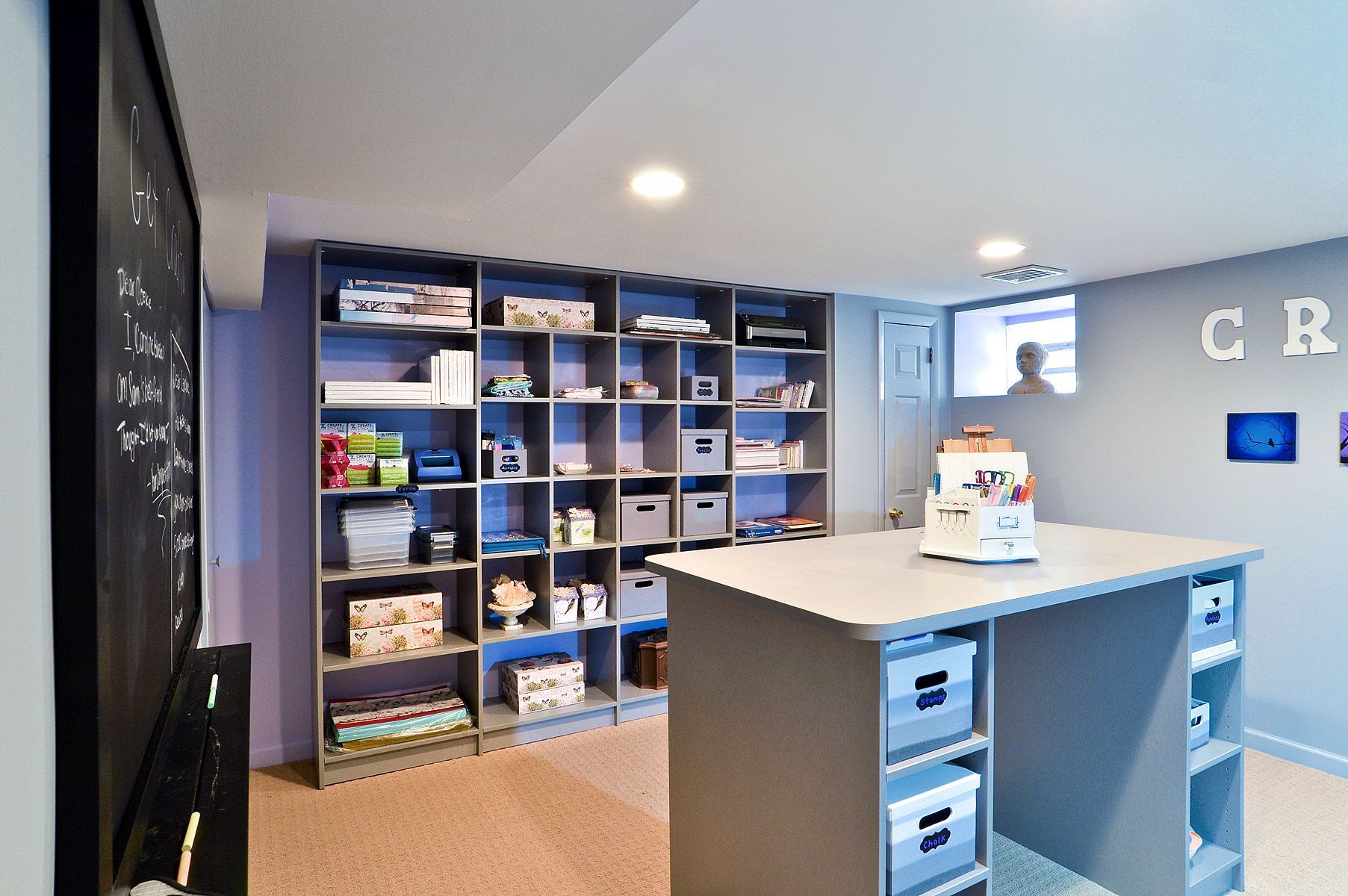 Blue-and-gray office or classroom with shelves, cubbies, and a central counter under recessed lights