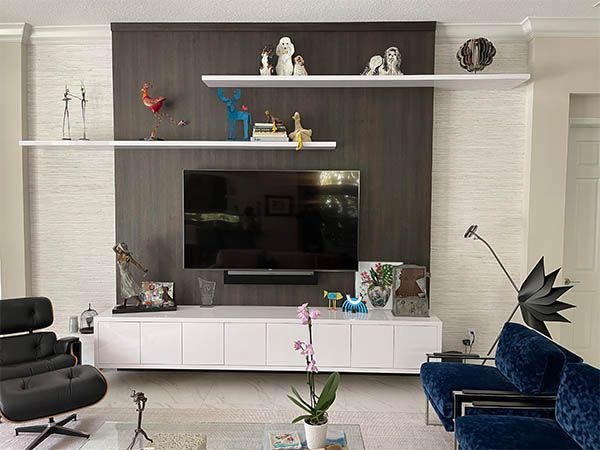 Modern living room with wall-mounted TV, white cabinets, blue sofa, black chair, and decorative shelves