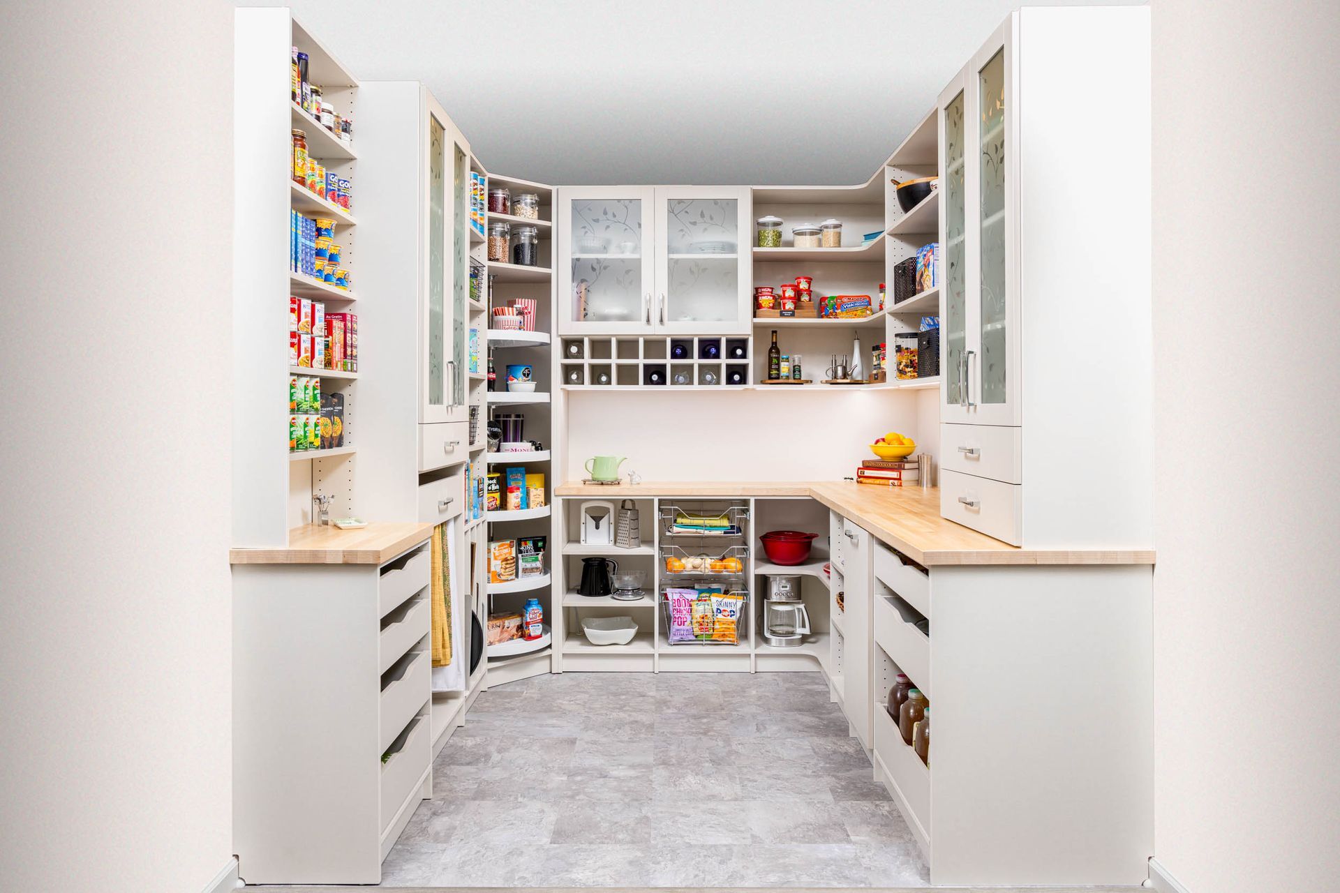 Bright white walk-in pantry with shelves, drawers, and organized snacks and jars.