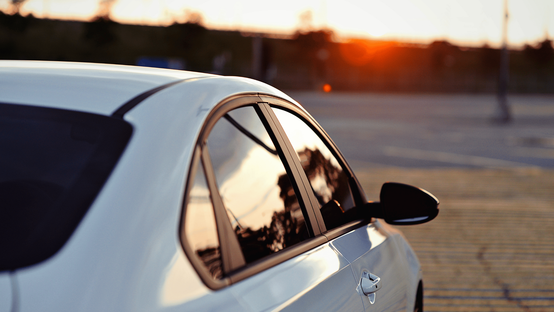A white car is parked on the side of the road at sunset.