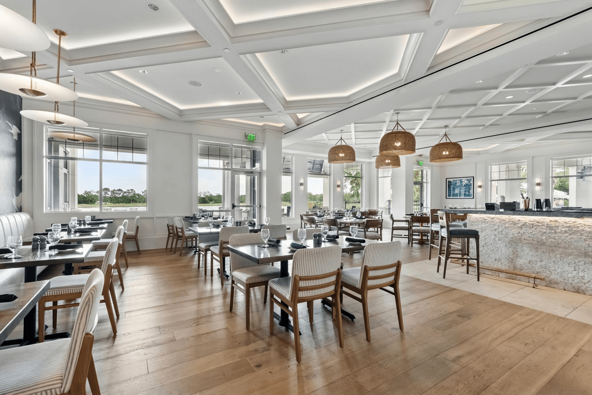 Elegant, bright restaurant interior with light wood floors, tables, and stylish lighting.