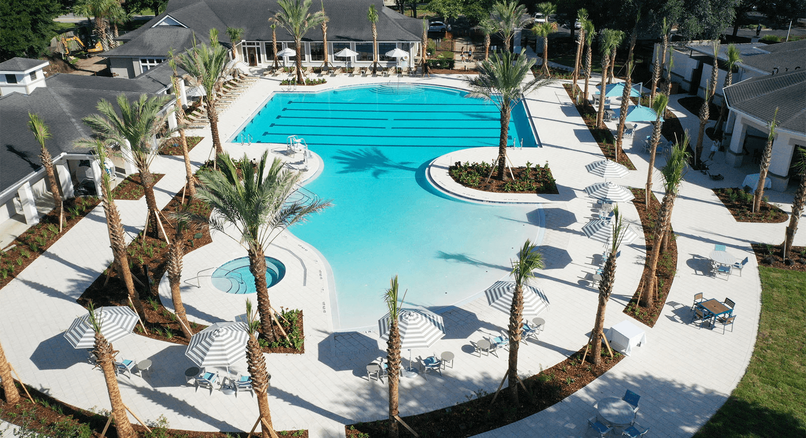 Aerial view of a large swimming pool complex with palm trees and a white concrete deck.