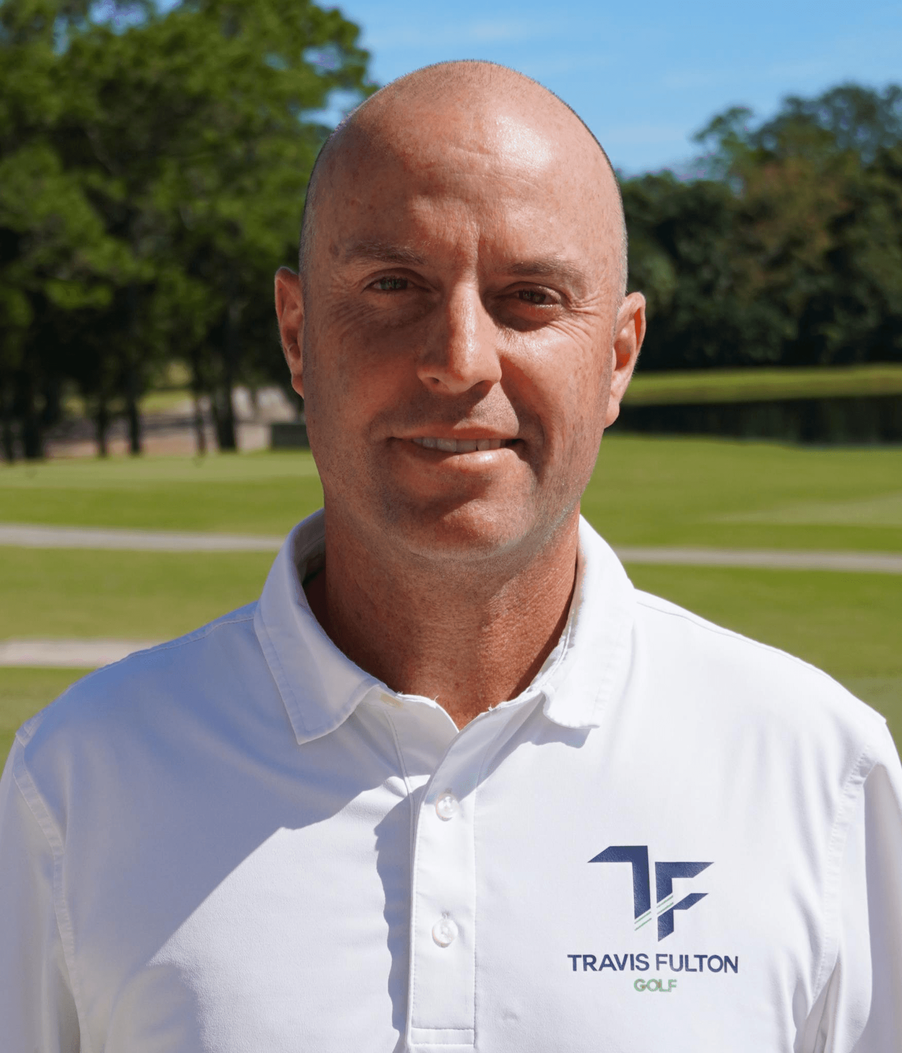 Tennis player in white shorts and visor swings racket on green court, shadow visible.