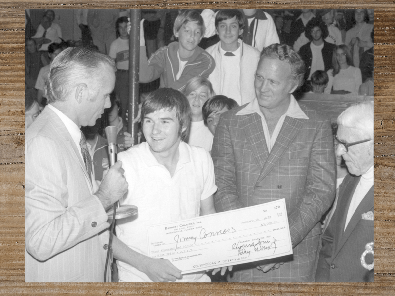 Man receives a large check from another man, with a crowd in the background.
