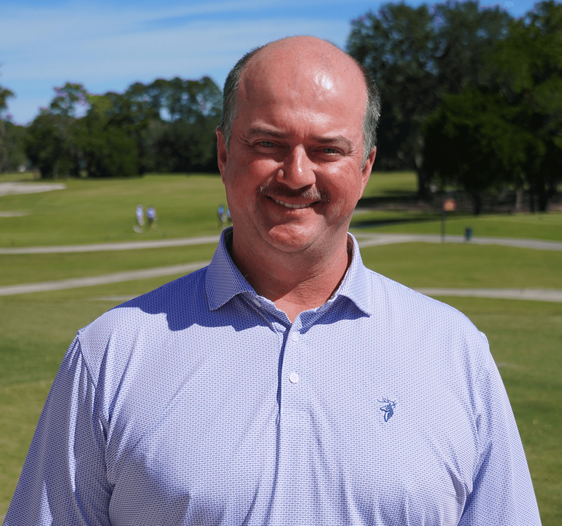 Tennis player in white shorts and visor swings racket on green court, shadow visible.