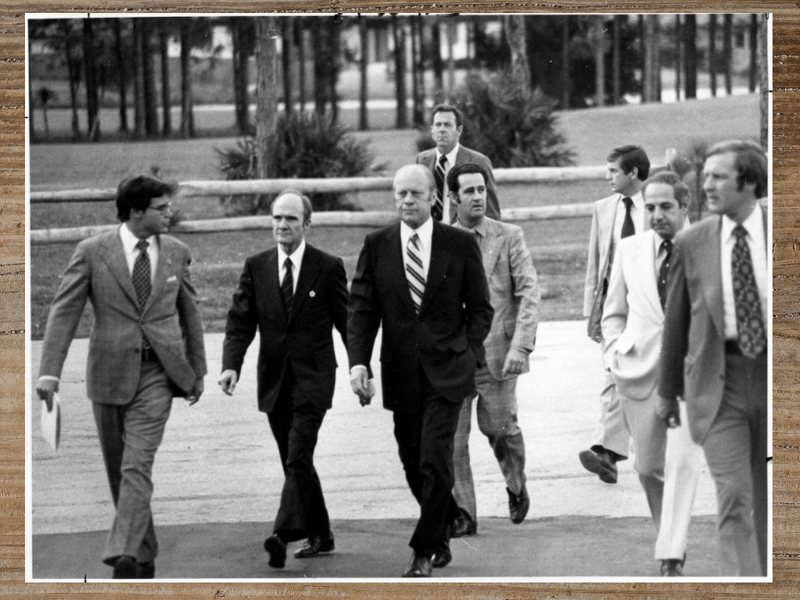 Gerald Ford and a group of men walking outside, a sunny day.
