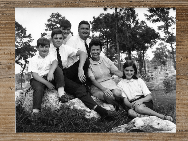 Family portrait, seven people seated on a rock outside.
