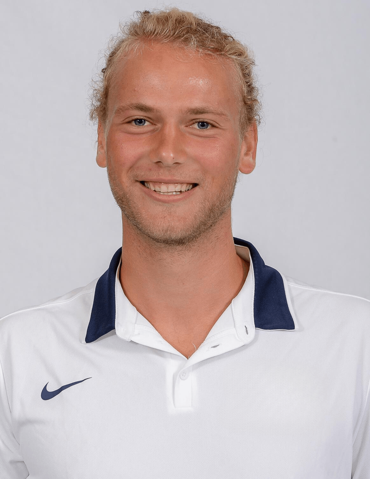 Tennis player in white shorts and visor swings racket on green court, shadow visible.