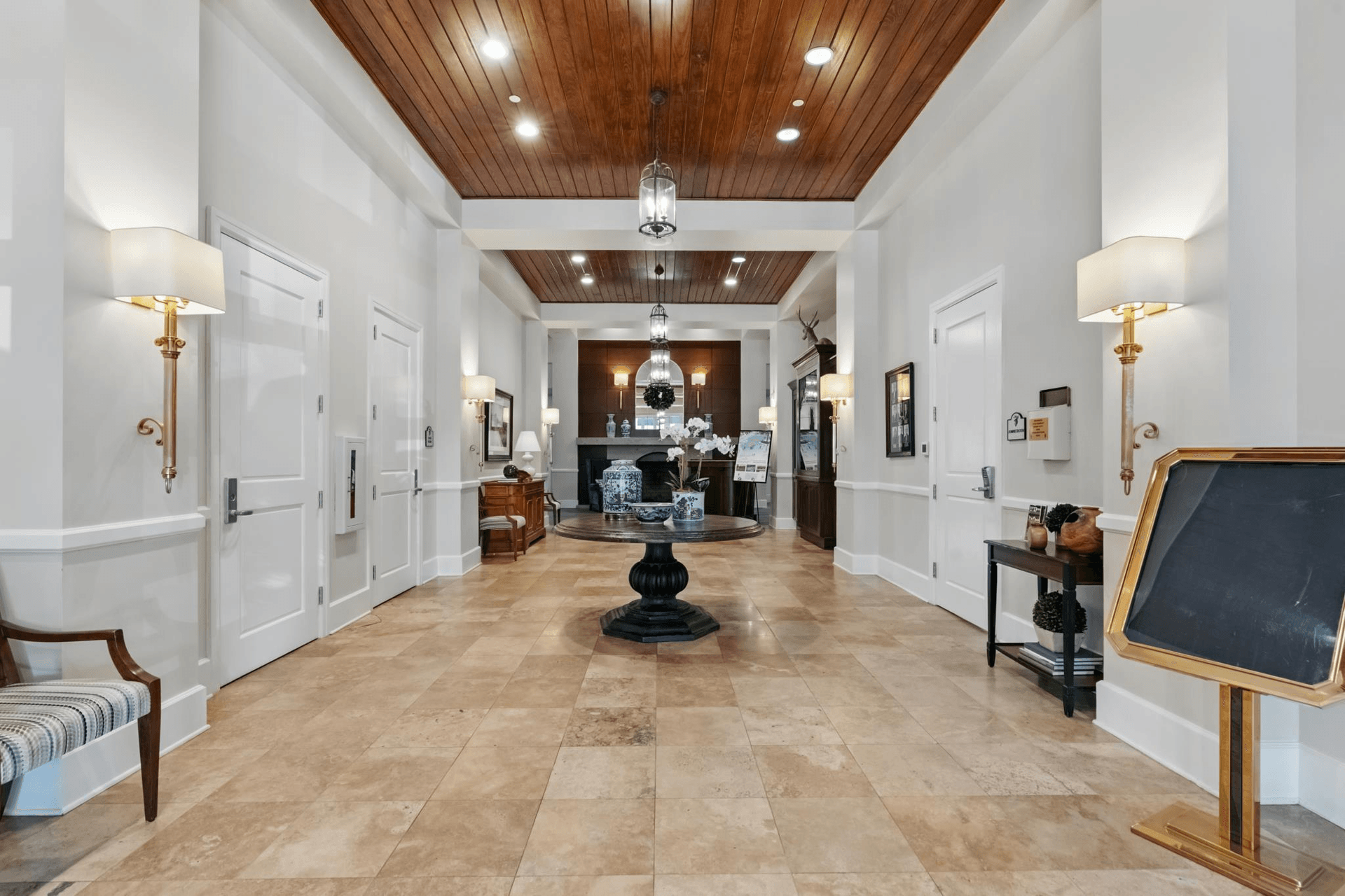 Elegant hallway with light-colored walls, tile floor, and a dark wooden ceiling. A table and chairs sit on the left.