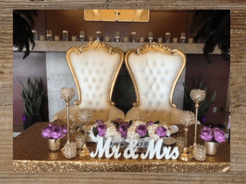 Wedding reception table with ornate gold chairs, gold sequins, floral arrangement, and 