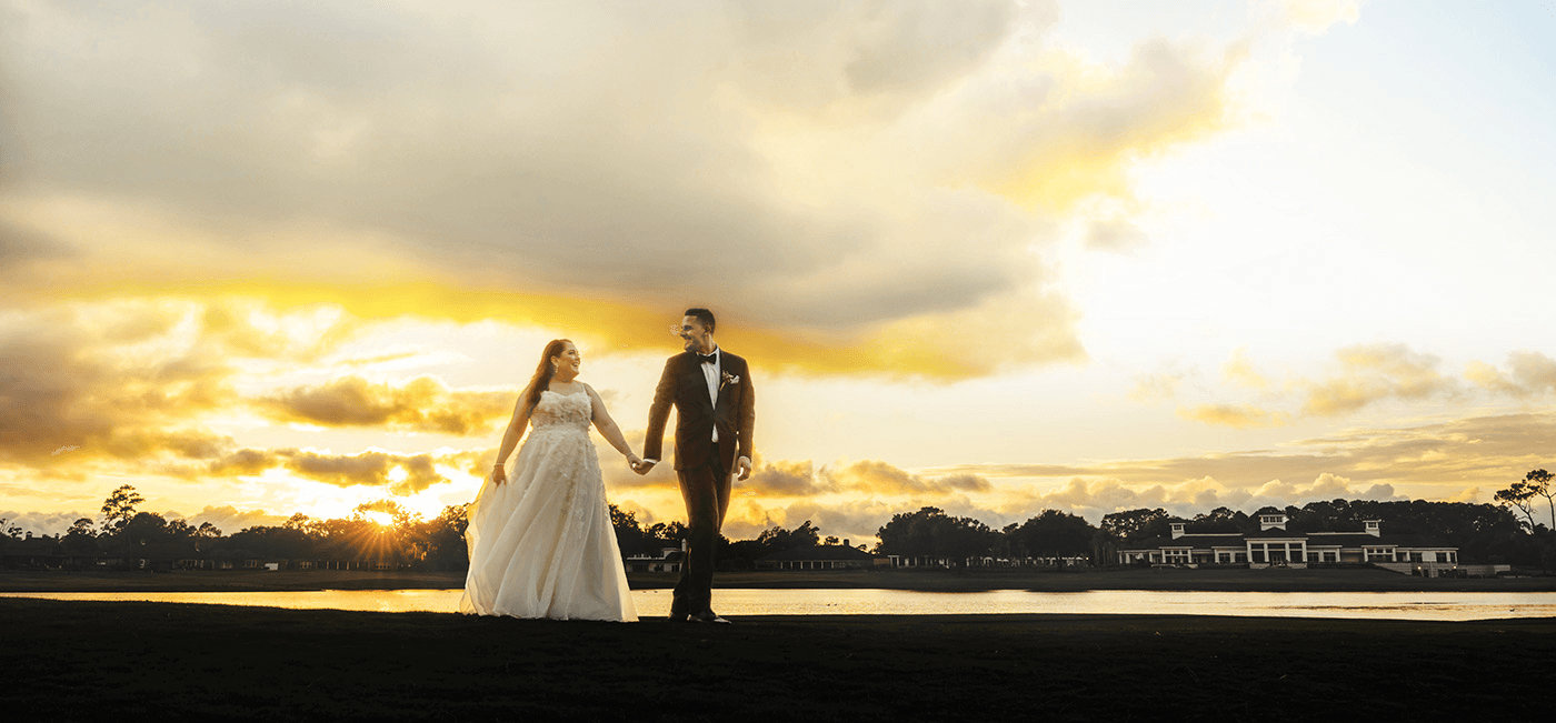 A bride and groom holding hands, silhouetted against a golden sunset.