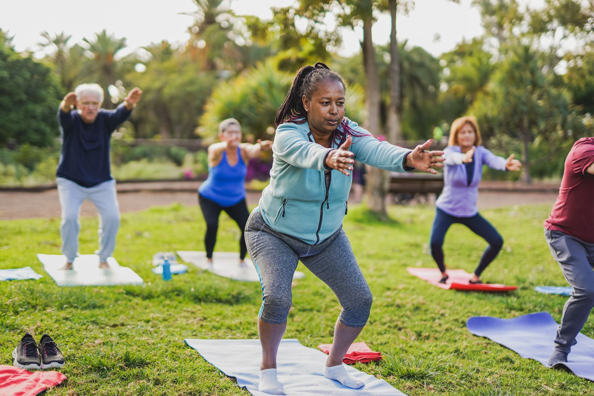 People exercising outdoors on yoga mats in a green park, doing a group fitness routine.