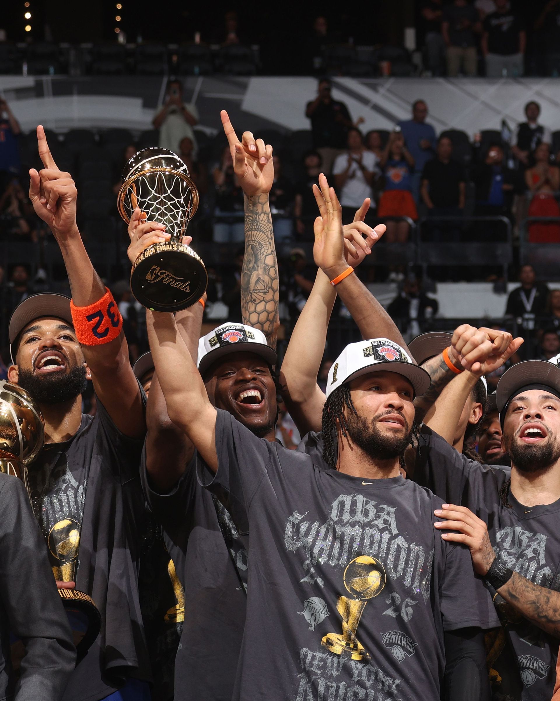 Basketball players in black shirts celebrate while holding up a championship trophy on court