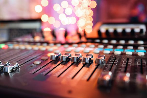 Sound mixing console with rows of sliders and colorful blurred lights in the background