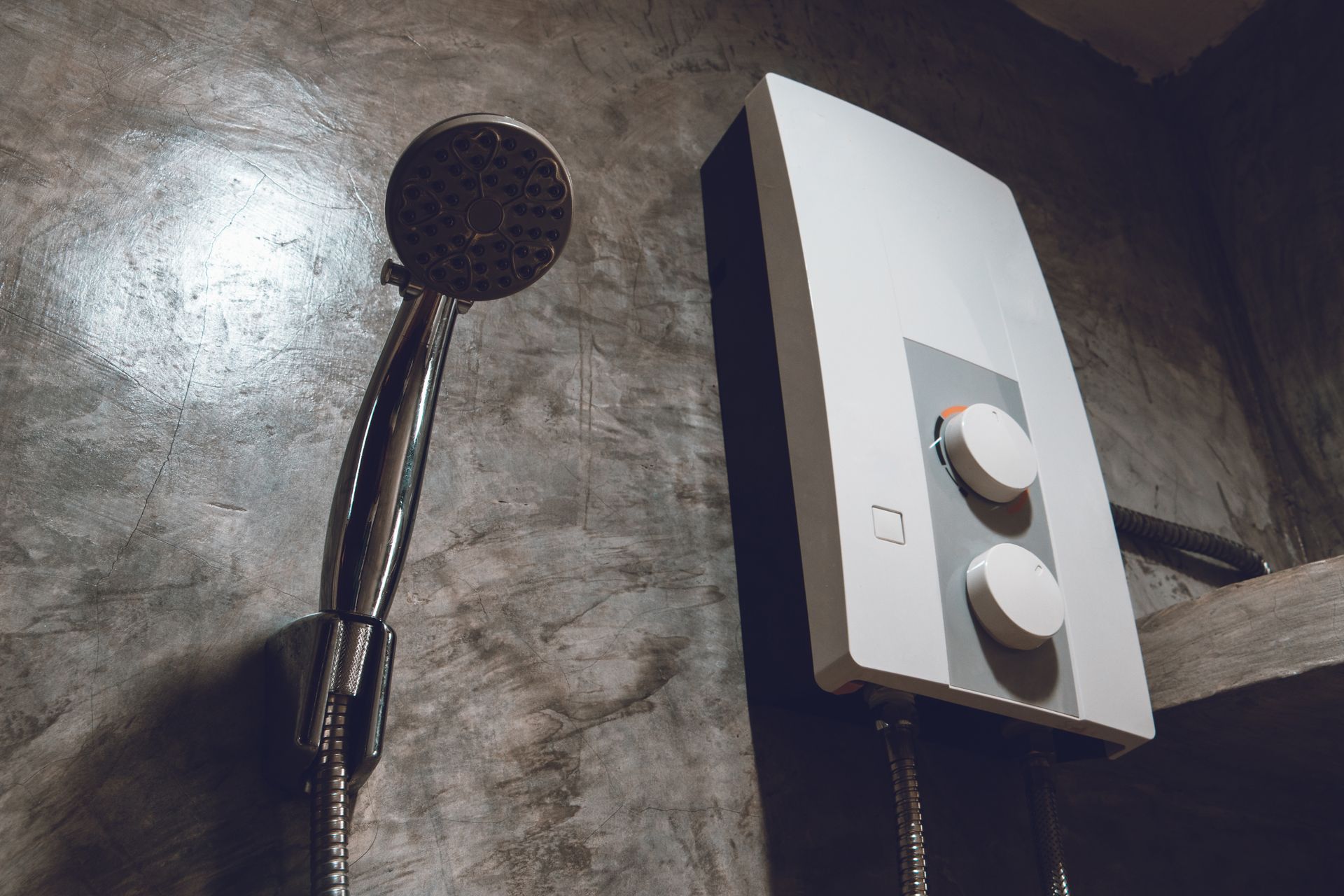 Shower area with handheld showerhead and white water heater against a concrete wall