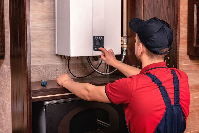 Technician in red overalls adjusting a wall-mounted boiler in a utility room