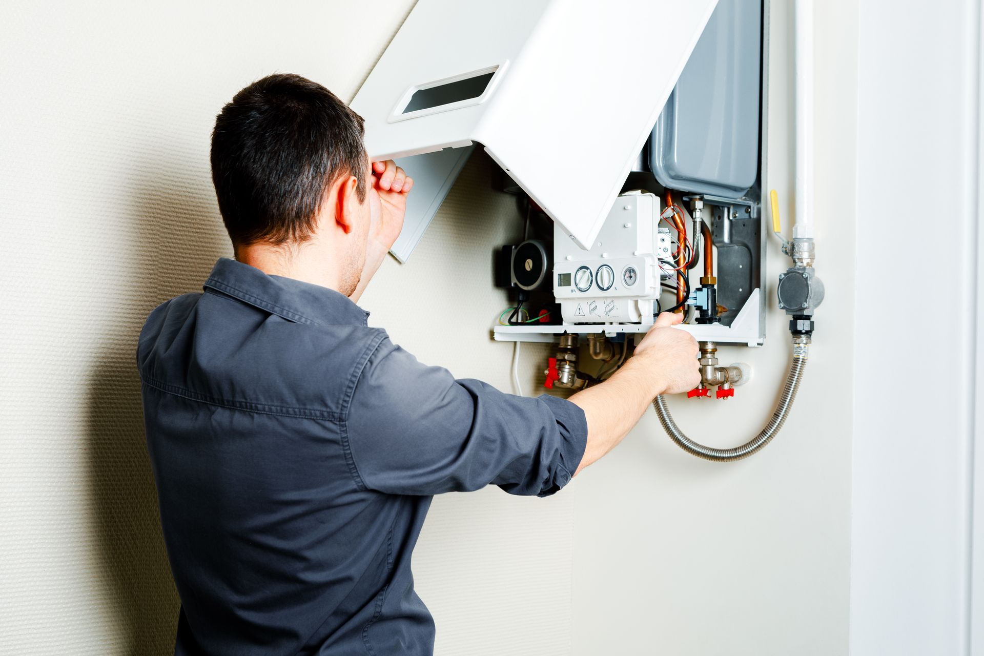Technician adjusting an open wall-mounted boiler with tools in a home interior.