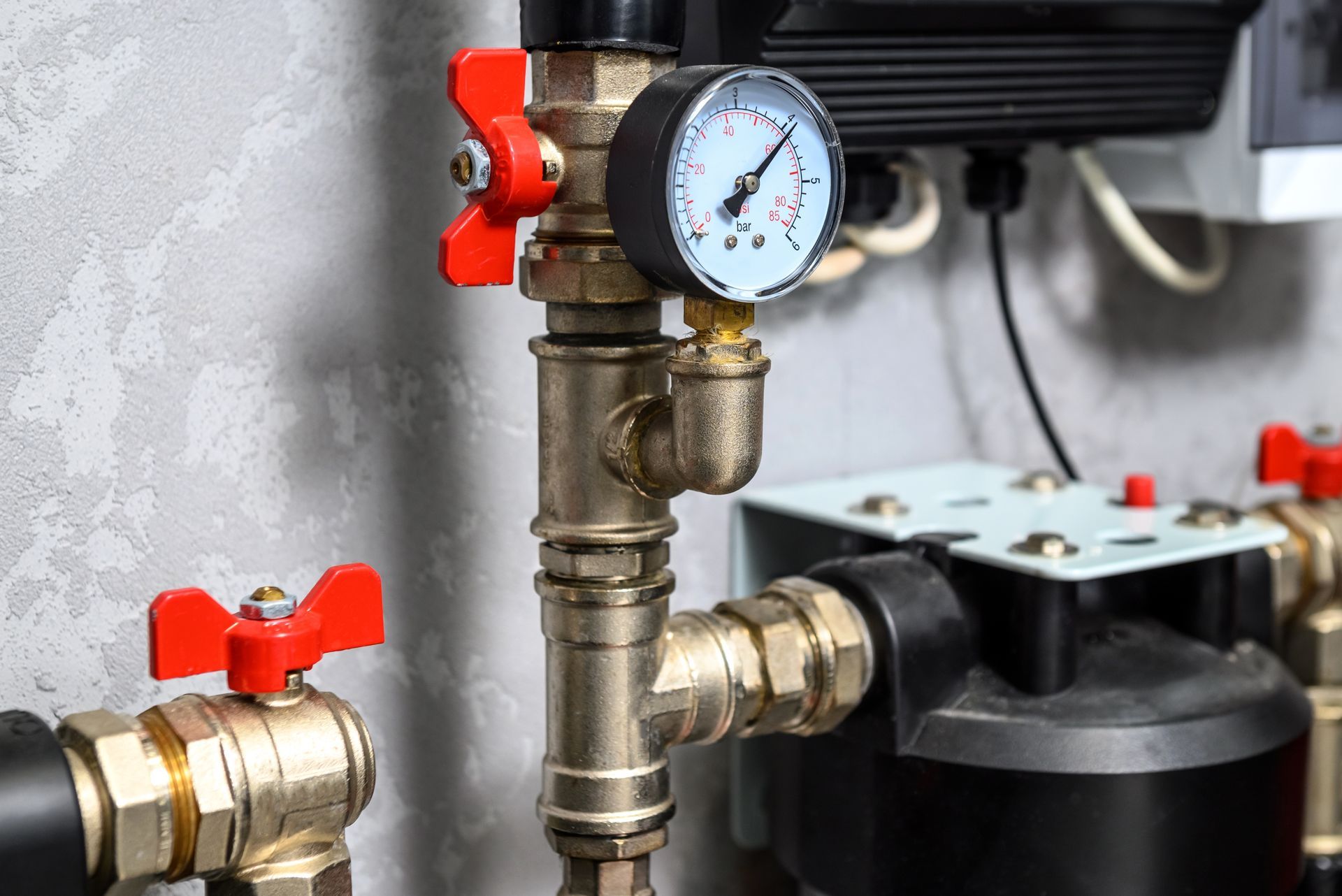 Pressure gauge and brass plumbing valves with red handles beside a black machine.
