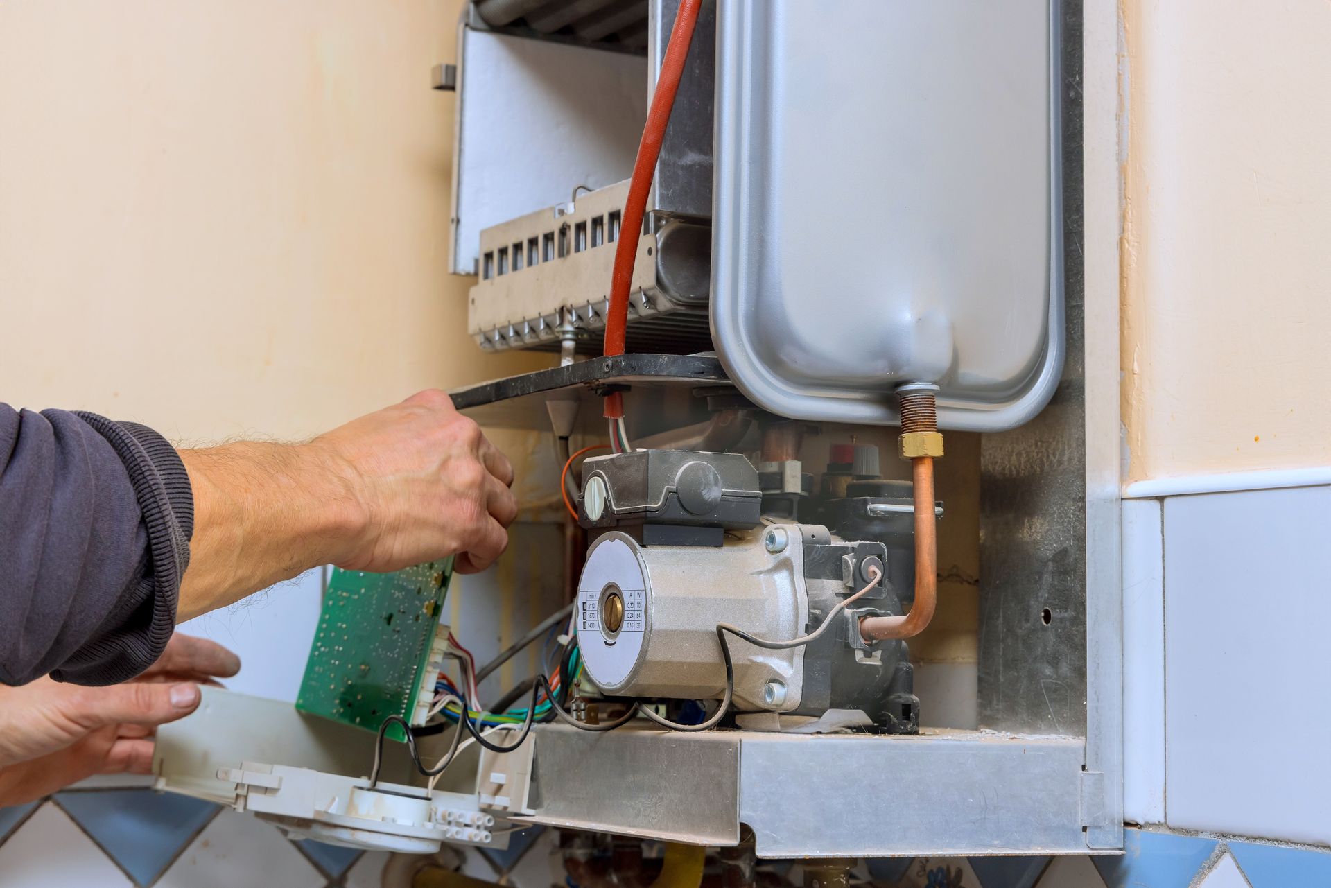 Technician inspecting wiring inside a wall-mounted boiler or HVAC unit