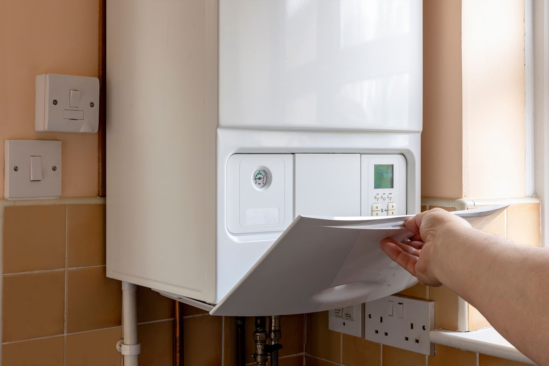 Hand opening a wall-mounted boiler panel in a tiled kitchen area