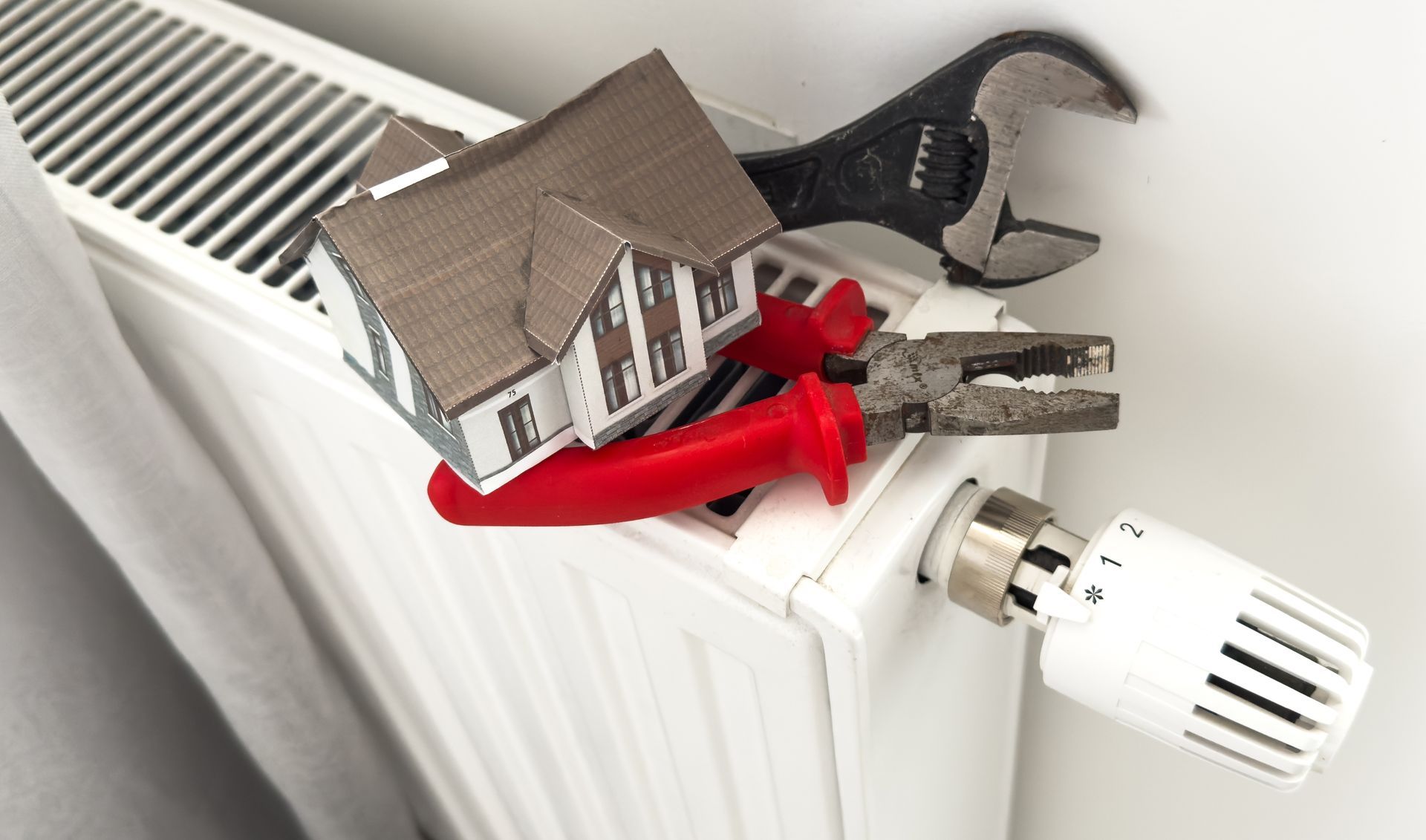 Red toy tools and a small house model on a white radiator next to a heating valve knob.