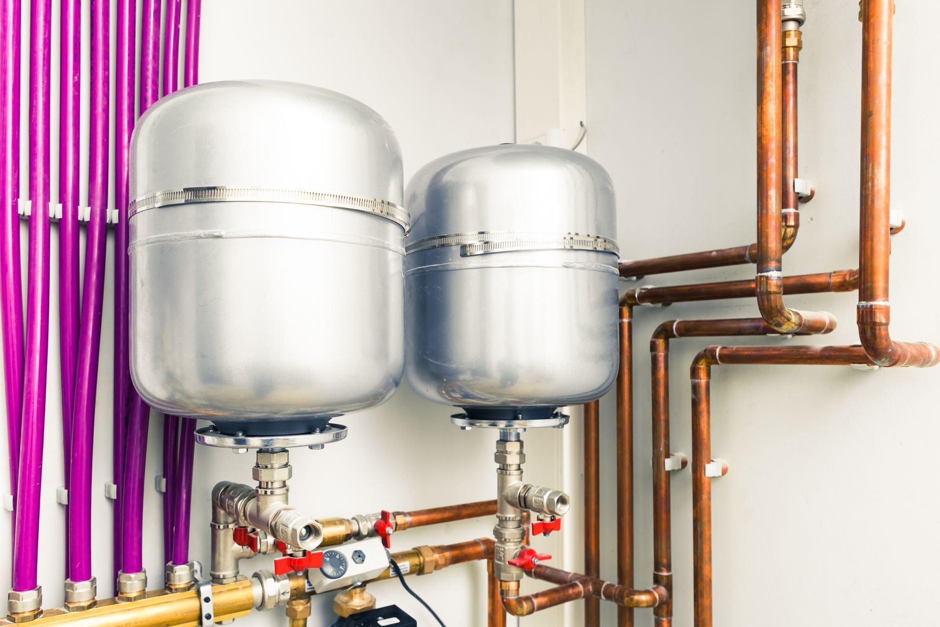 Two silver tanks with copper pipes and colorful conduit on a utility wall