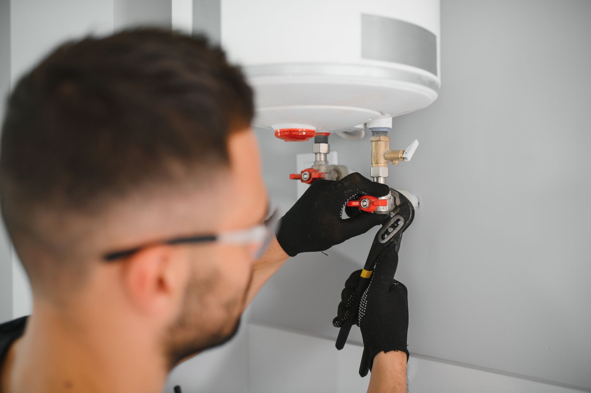 Technician inspecting wiring under a white ceiling-mounted device with a tool.
