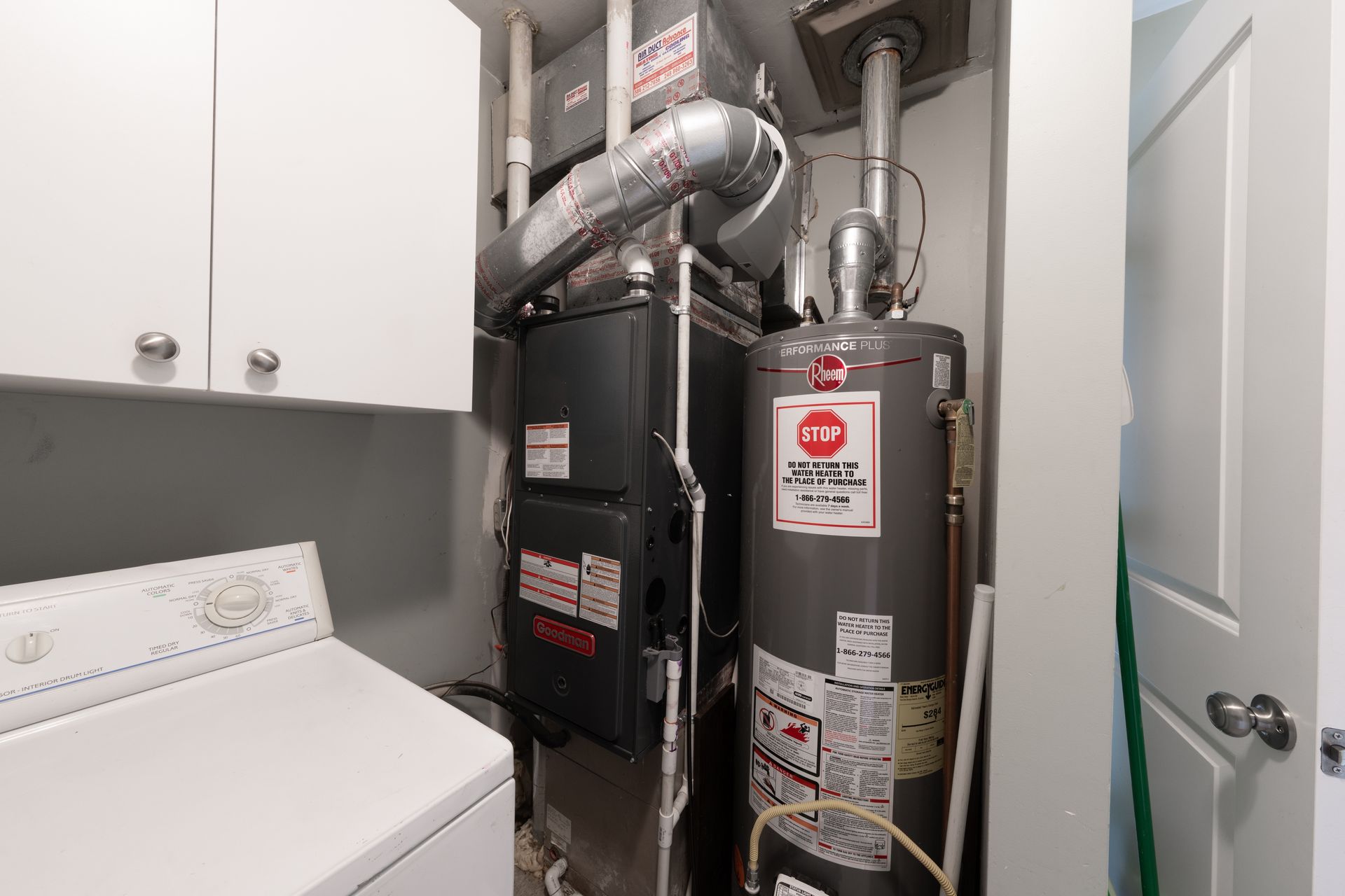 Laundry room with stacked washer and dryer beside a furnace and water heater in a narrow utility closet