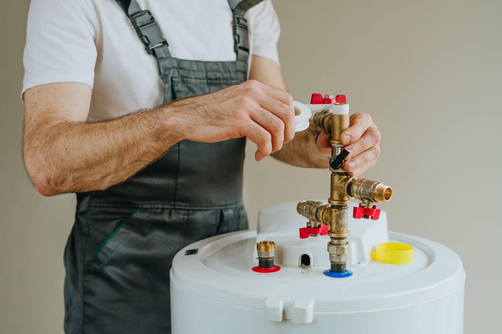 Plumber tightening a faucet on a white water heater tank with red and yellow valves