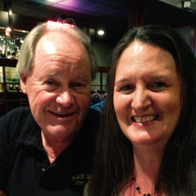 Two people smiling in a dimly lit restaurant bar with warm and purple lights