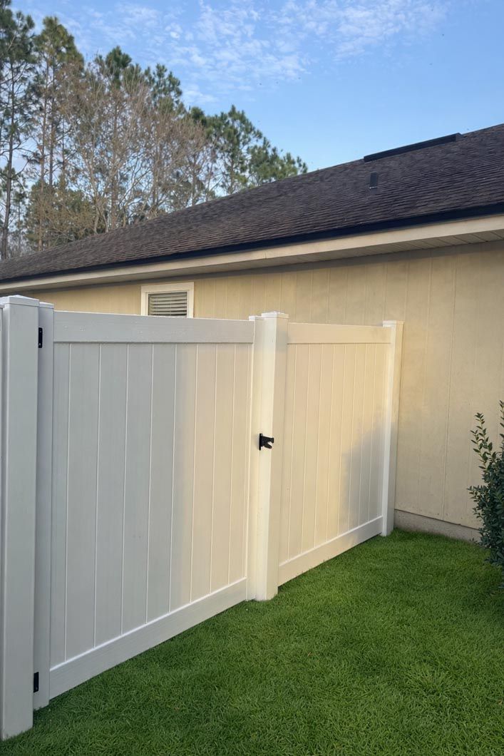 White vinyl fence and gate beside a beige house on a green lawn under a blue sky