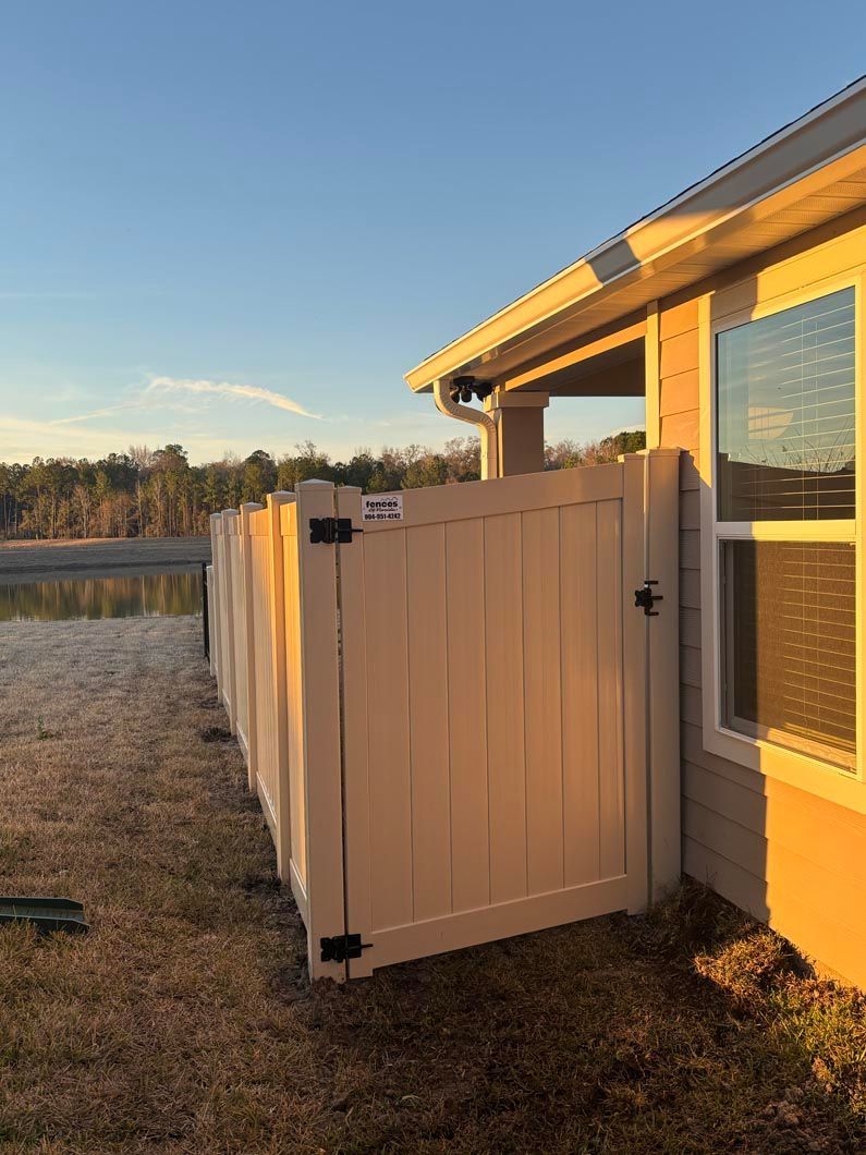 White gate beside a yellow house at sunset, opening to a grassy yard with fields in the background