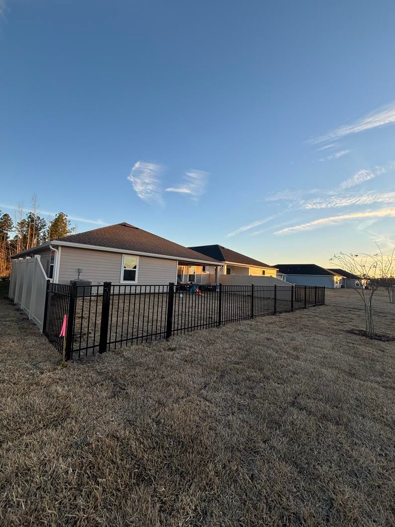 Single-story homes behind a black fence on a dry hillside at sunset under a clear blue sky