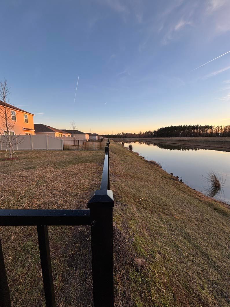 Riverbank path at sunset with calm water, grassy slope, and a building on the left.